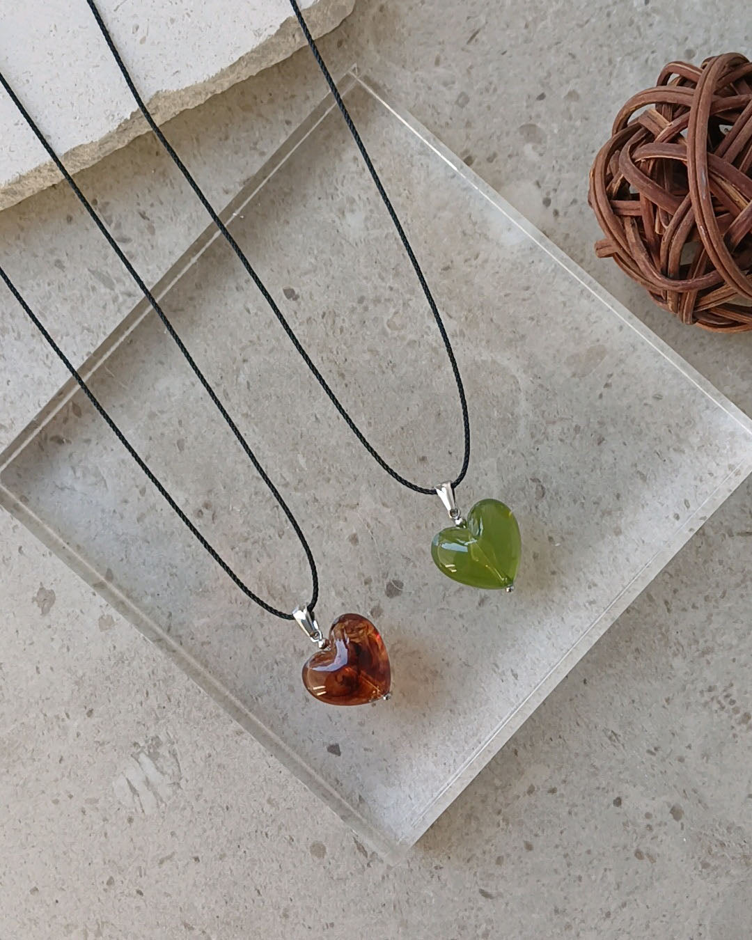 Two heart-shaped pendants on black cords with a neutral background