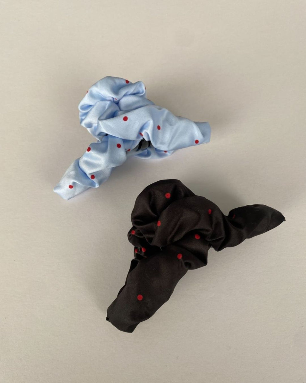 Close-up profile of a light blue and a black satin fabric-wrapped jaw clip with a red polka dot pattern on a plain white surface.