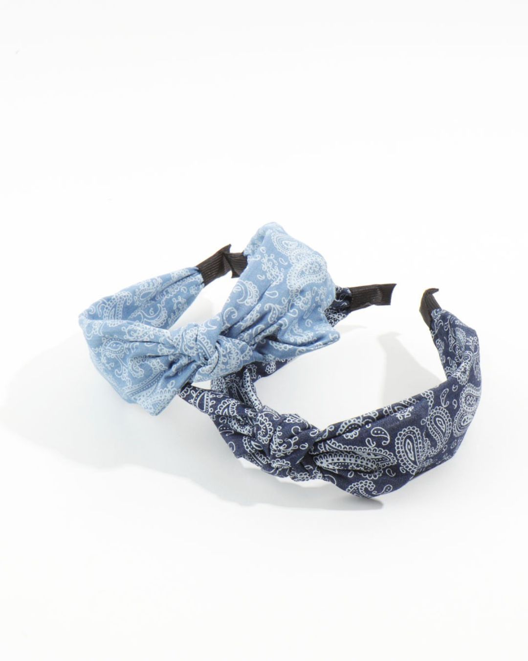 Two soft fabric knotted headbands in light blue and dark blue bandana prints overlapping on a bright white surface.