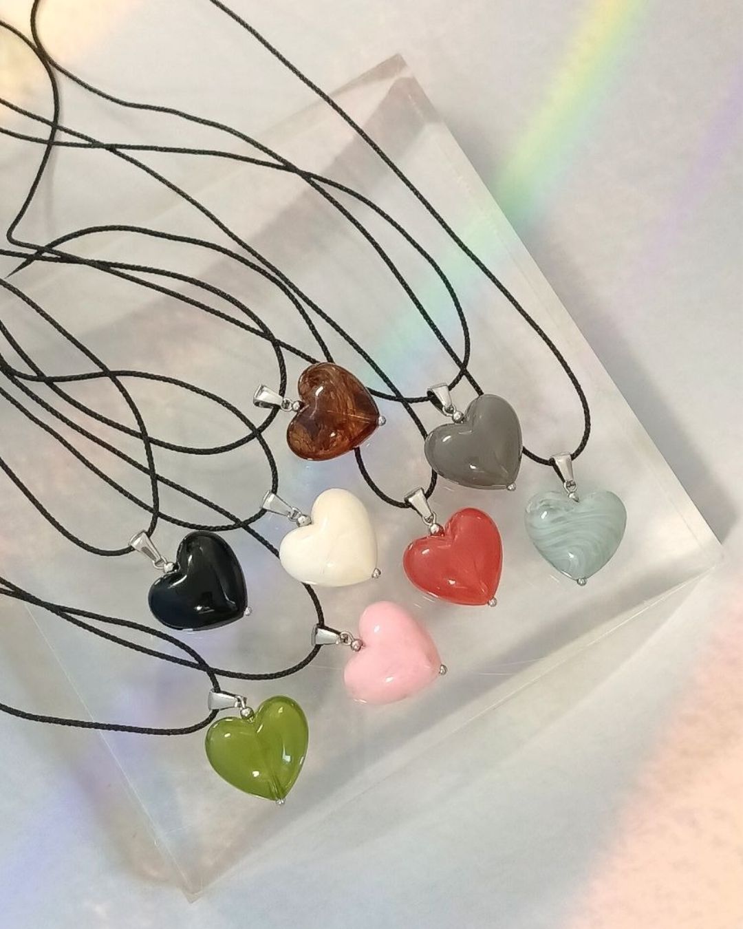 Set of heart-shaped pendant necklaces on a white surface with a rainbow effect.