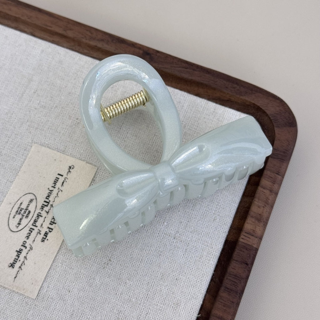 A periwinkle blue glossy acrylic bow claw clip displayed on a white textured fabric background with a wooden frame.