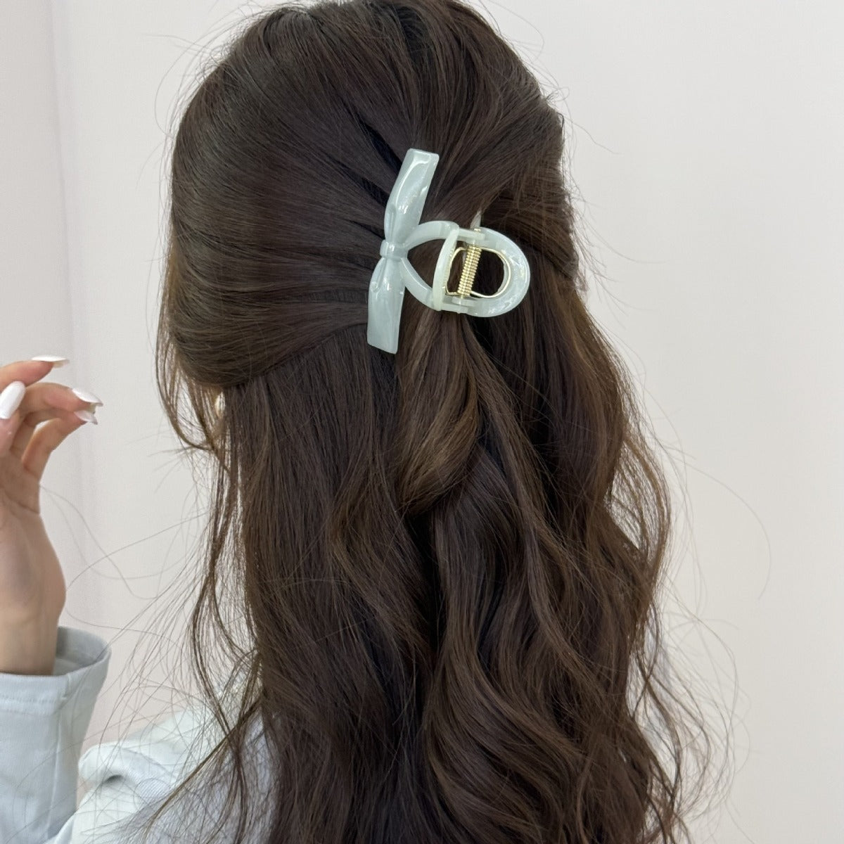 Back view of a woman with long, wavy brown hair styled in an elegant half-updo, secured by a mint green pearlescent bow claw clip.