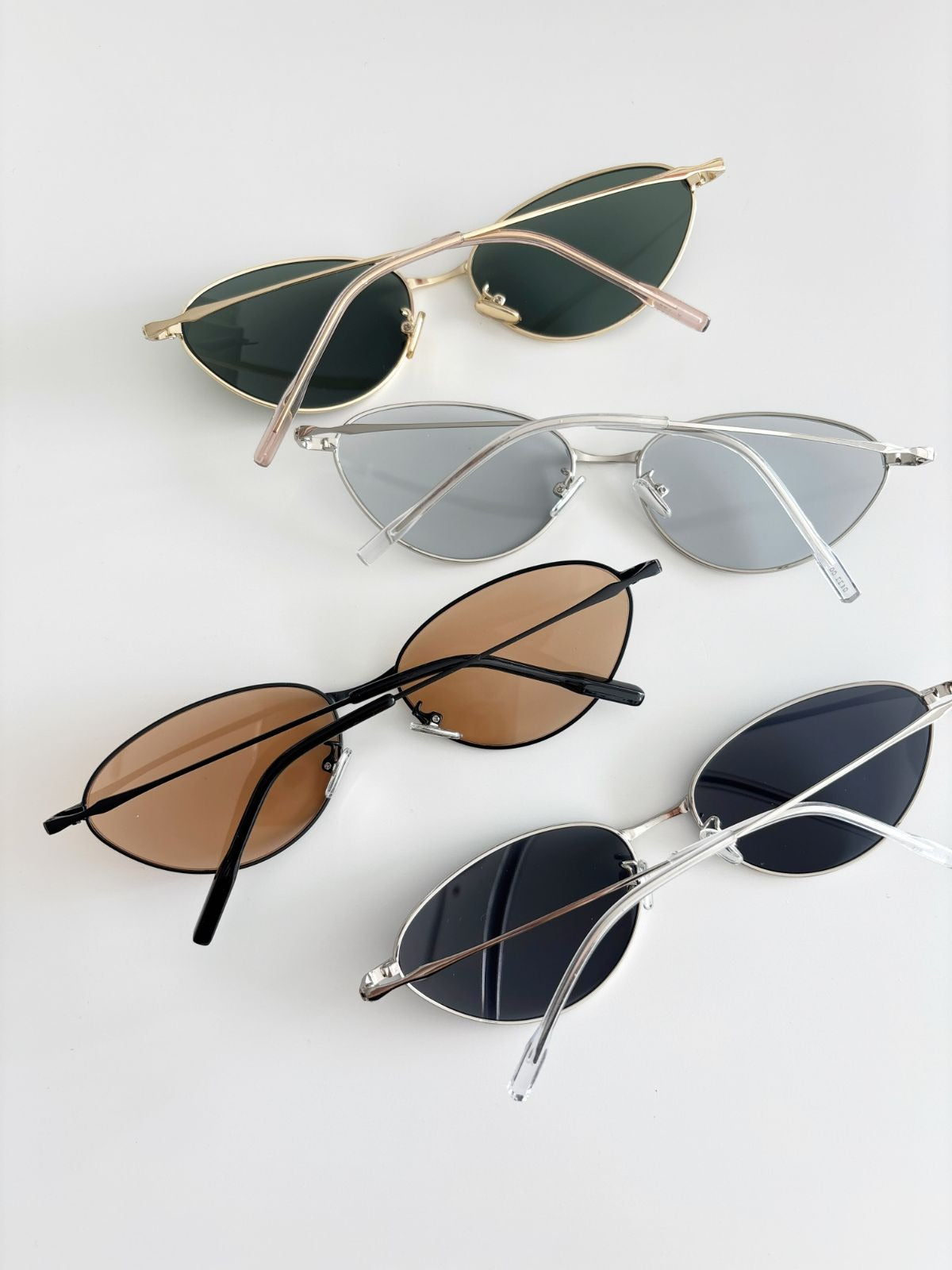 Four pairs of sunglasses with different lens colors and frames on a light gray background