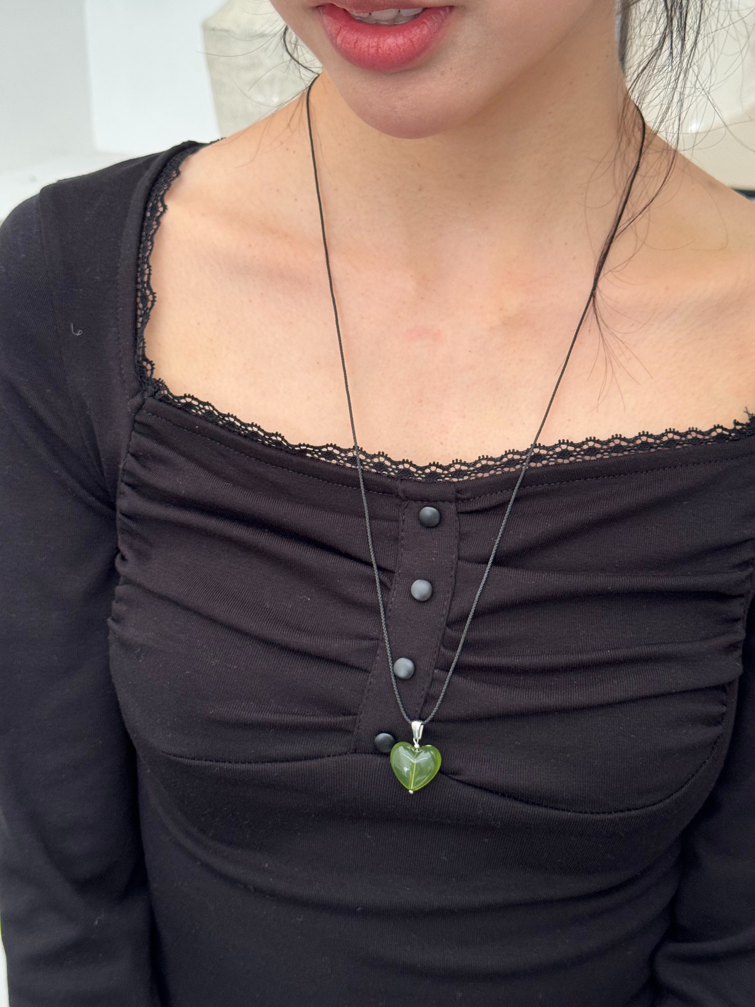 Person wearing a black top with a green heart-shaped pendant necklace.