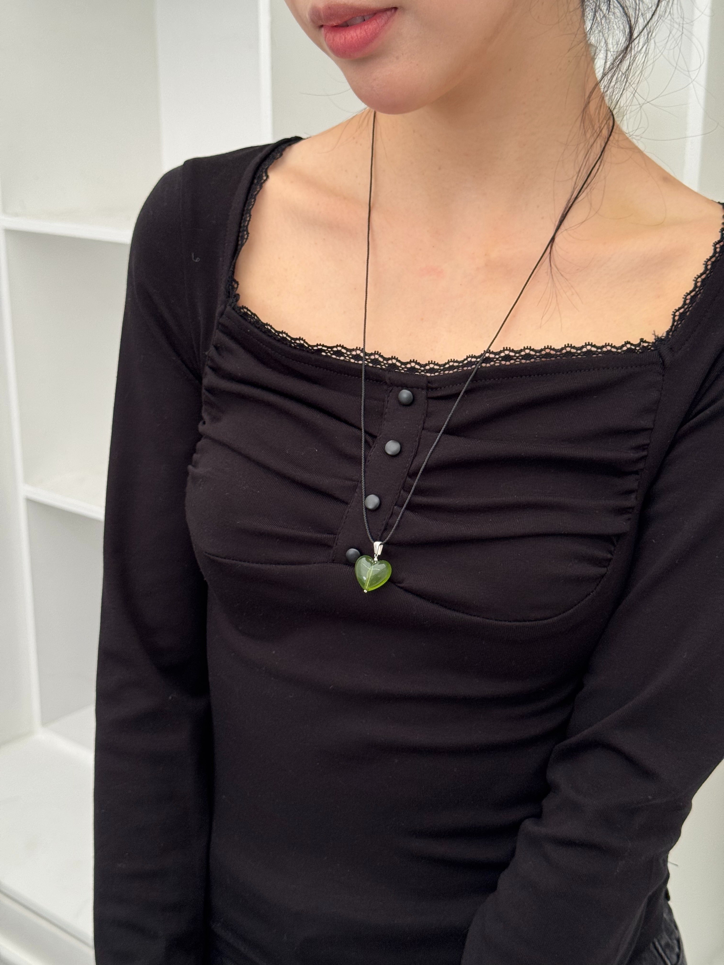 Person wearing a black top with a necklace featuring a green heart pendant.