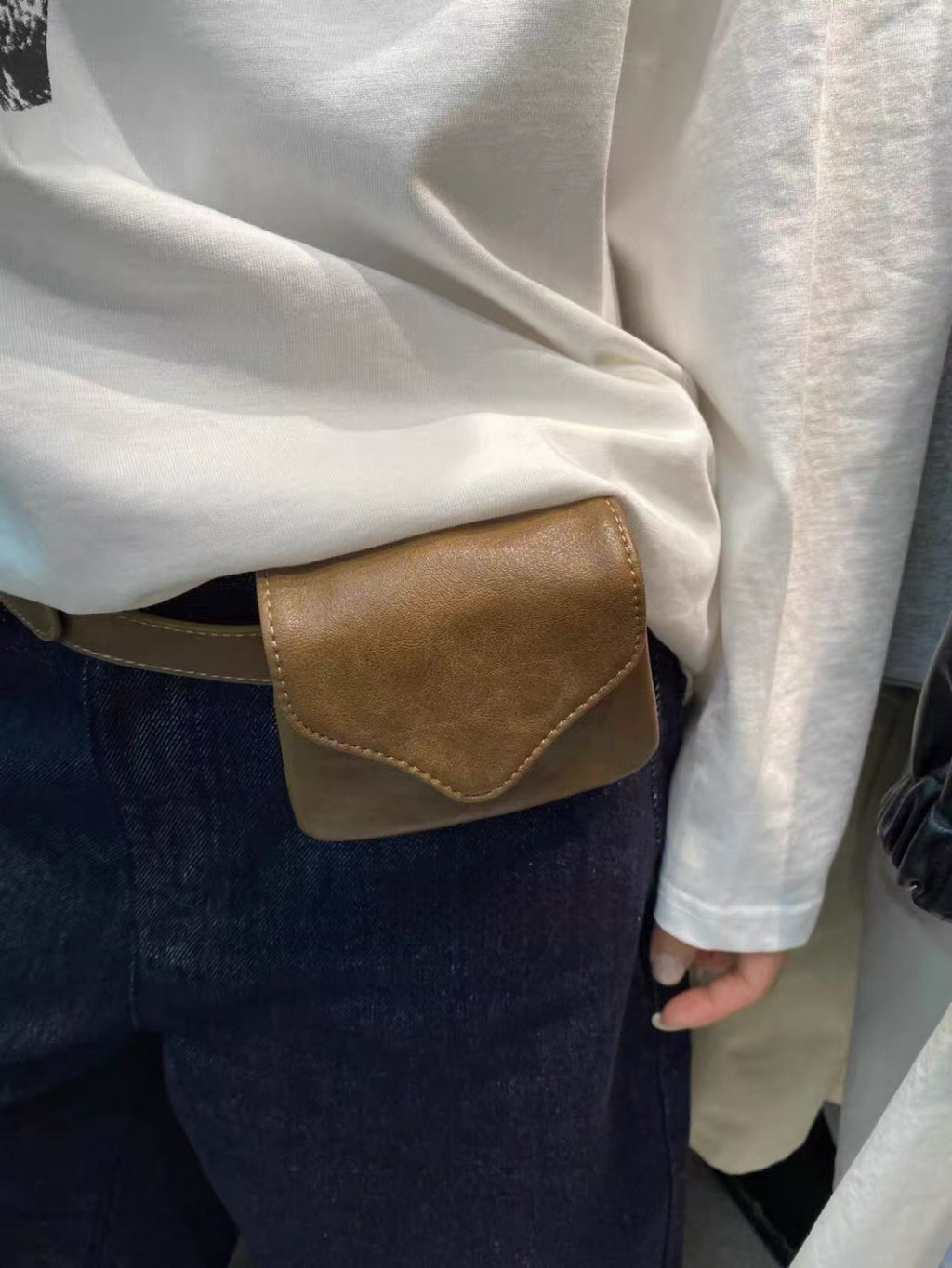 Person wearing a white shirt with a brown leather patch pocket and dark pants.