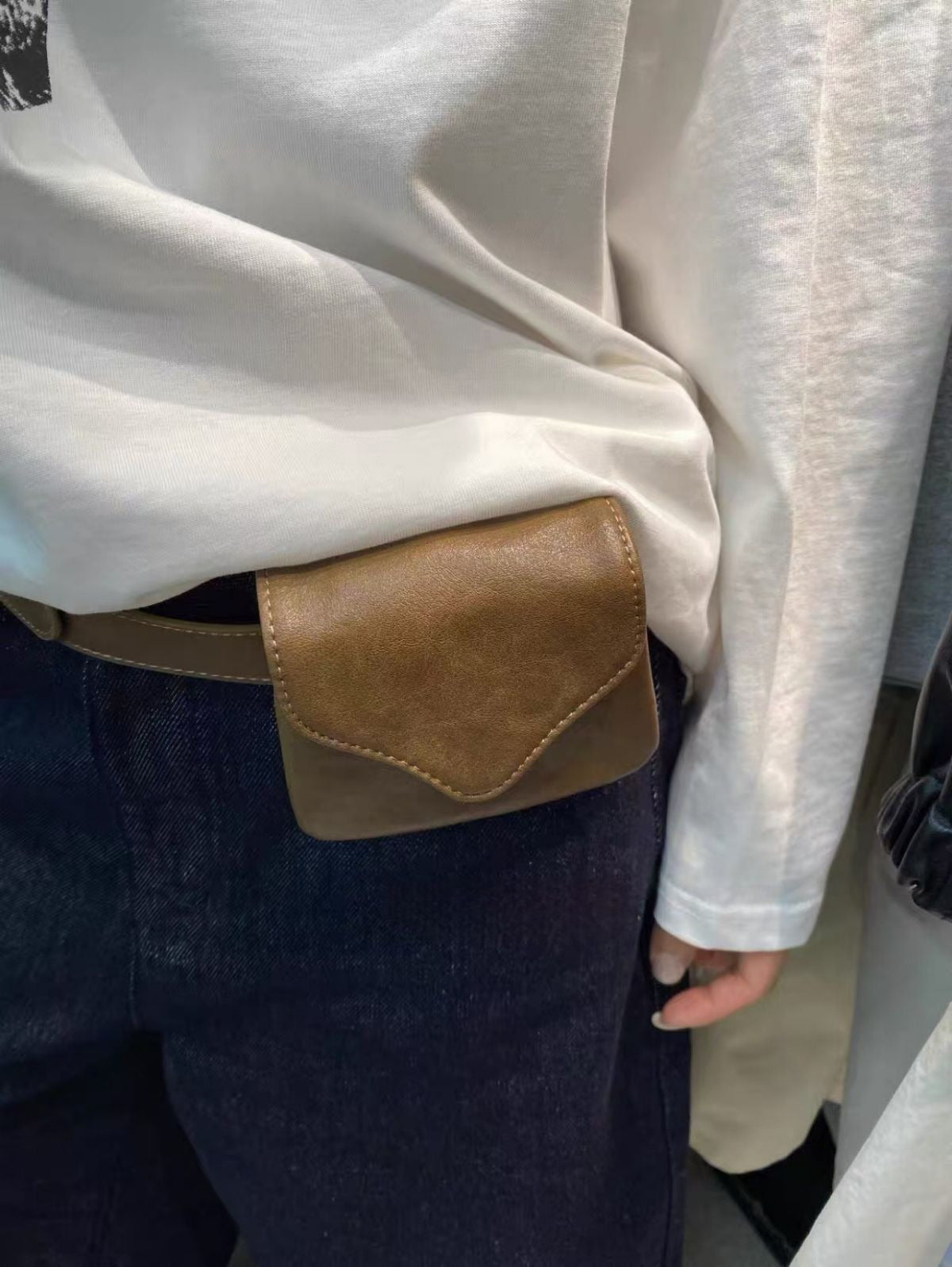 Person wearing a white shirt with a brown leather patch pocket and dark pants.