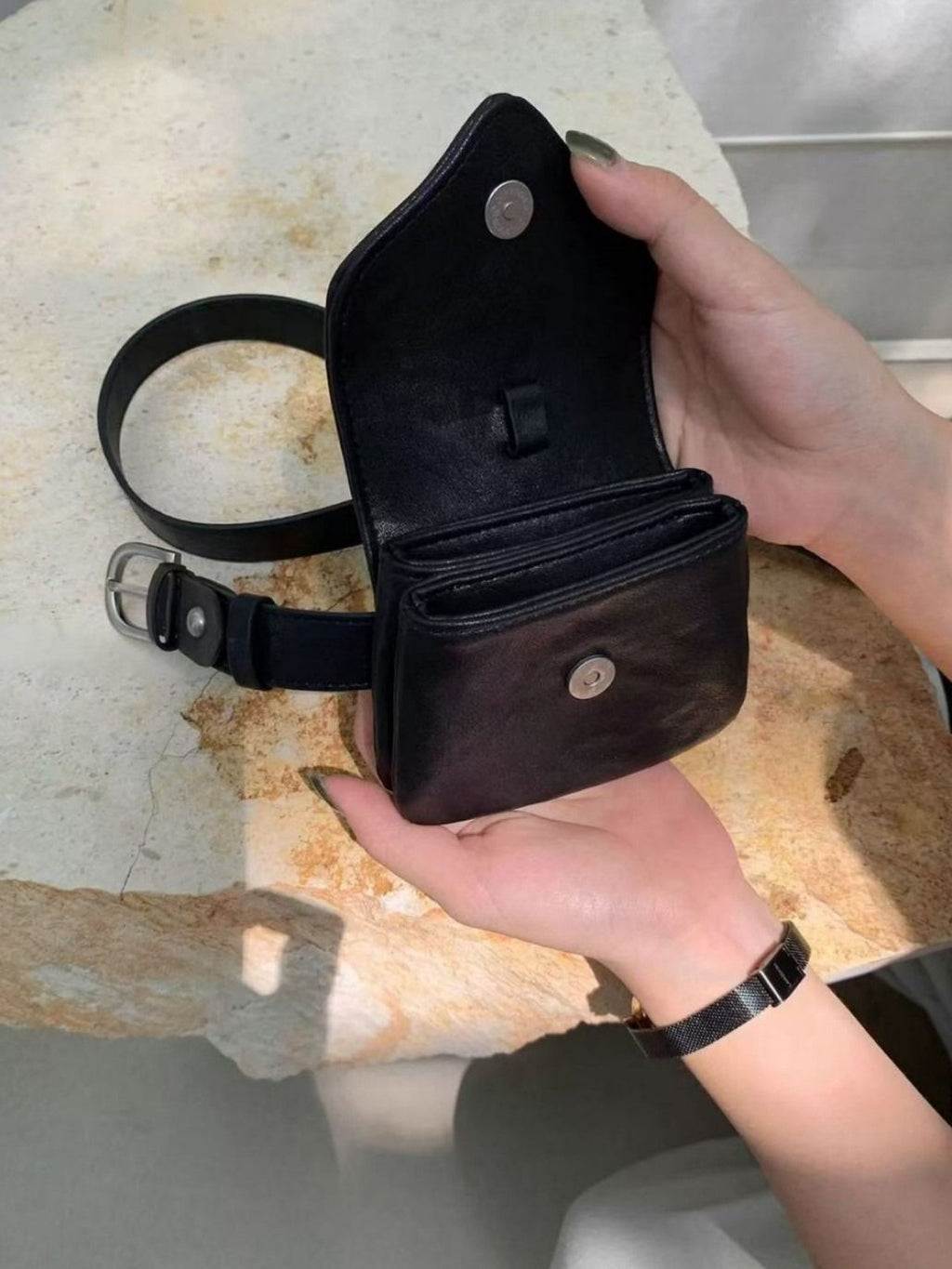 Black leather pouch held by a hand on a textured surface