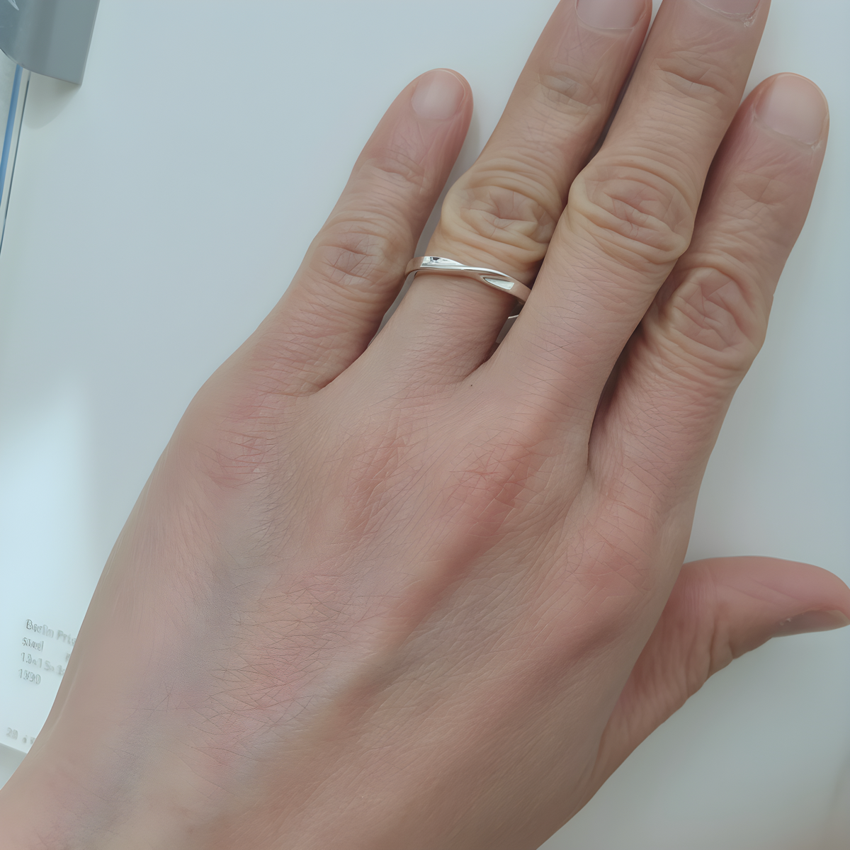 A person's hand wearing a sleek silver sculptural twist ring on their middle finger against a clean white background.