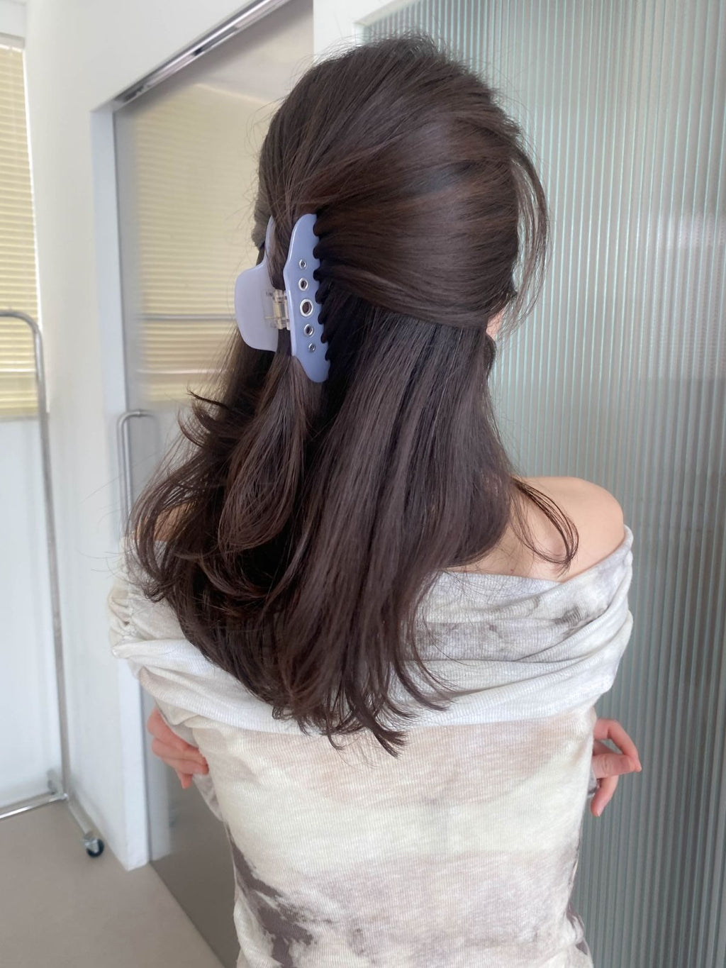 Back view of a woman wearing a light lavender purple grommet hair claw clip to hold her thick, dark wavy hair in a half-up, half-down hairstyle.