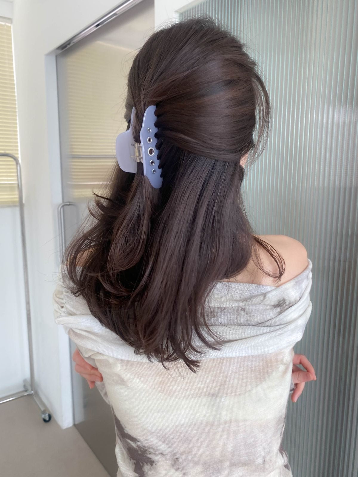 Back view of a woman wearing a light lavender purple grommet hair claw clip to hold her thick, dark wavy hair in a half-up, half-down hairstyle.