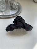 Black satin ruched hair claw clip with red polka dots sitting on a white countertop next to a silver serving tray with drinking glasses.