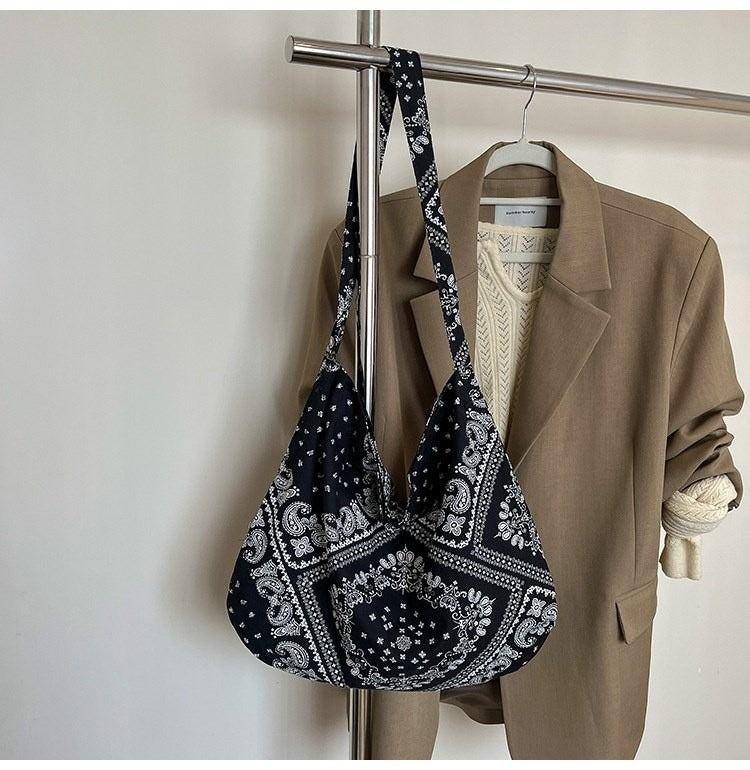 Black patterned bag, beige blazer, and white sweater on a rack against a plain background