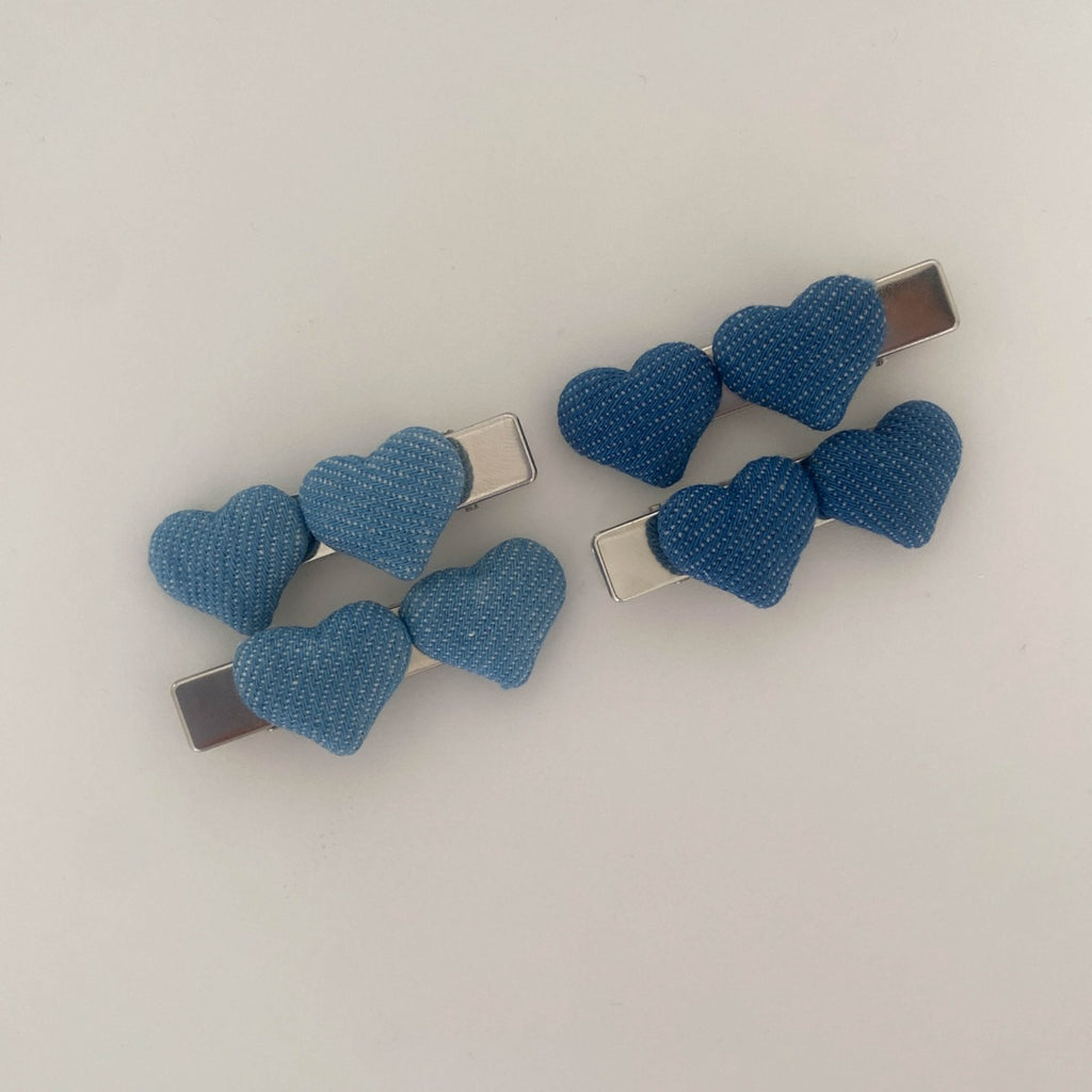 Four puffy denim heart alligator barrettes displayed on a textured beige fabric next to a white plate and a magazine featuring green grapes.