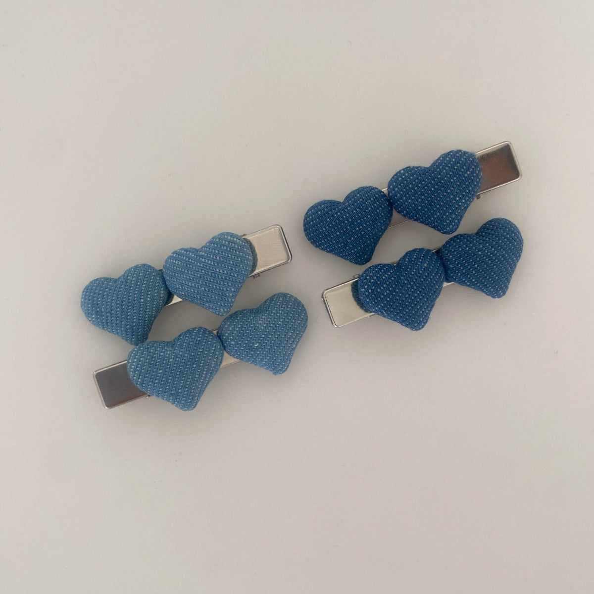 Four puffy denim heart alligator barrettes displayed on a textured beige fabric next to a white plate and a magazine featuring green grapes.