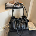 Black ruched dumpling shoulder bag with a black star keychain attached, sitting gracefully next to a stack of decorative aesthetic books.