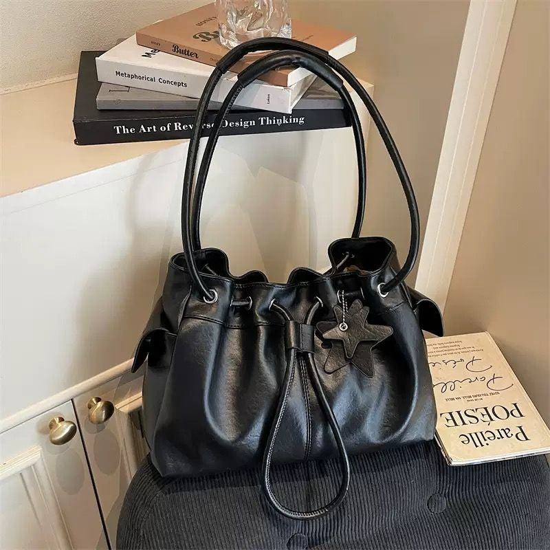Black ruched dumpling shoulder bag with a black star keychain attached, sitting gracefully next to a stack of decorative aesthetic books.