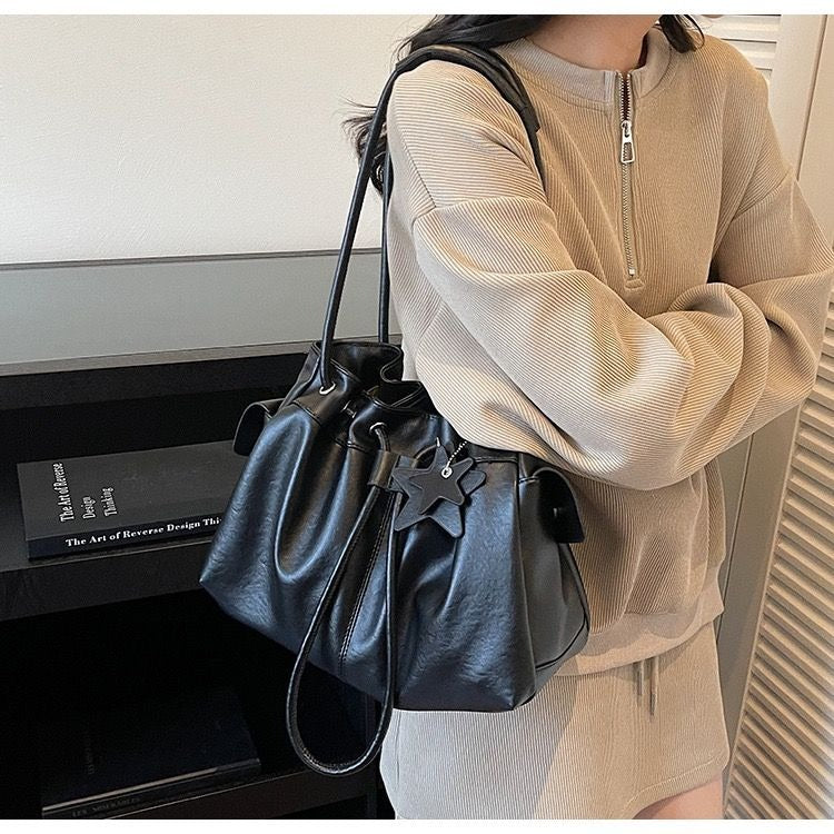 A woman wearing a beige ribbed quarter-zip sweater and skirt effortlessly carrying a black slouchy ruched shoulder bag under her arm.
