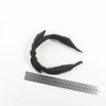 Top-down view of a black satin bow headband placed next to a silver metal measuring ruler to display its standard sizing scale.