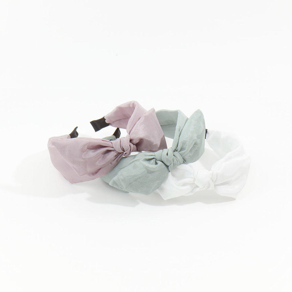 Three trendy soft satin headbands in dusty mauve, sage green, and white featuring an elegant top knot bow design.