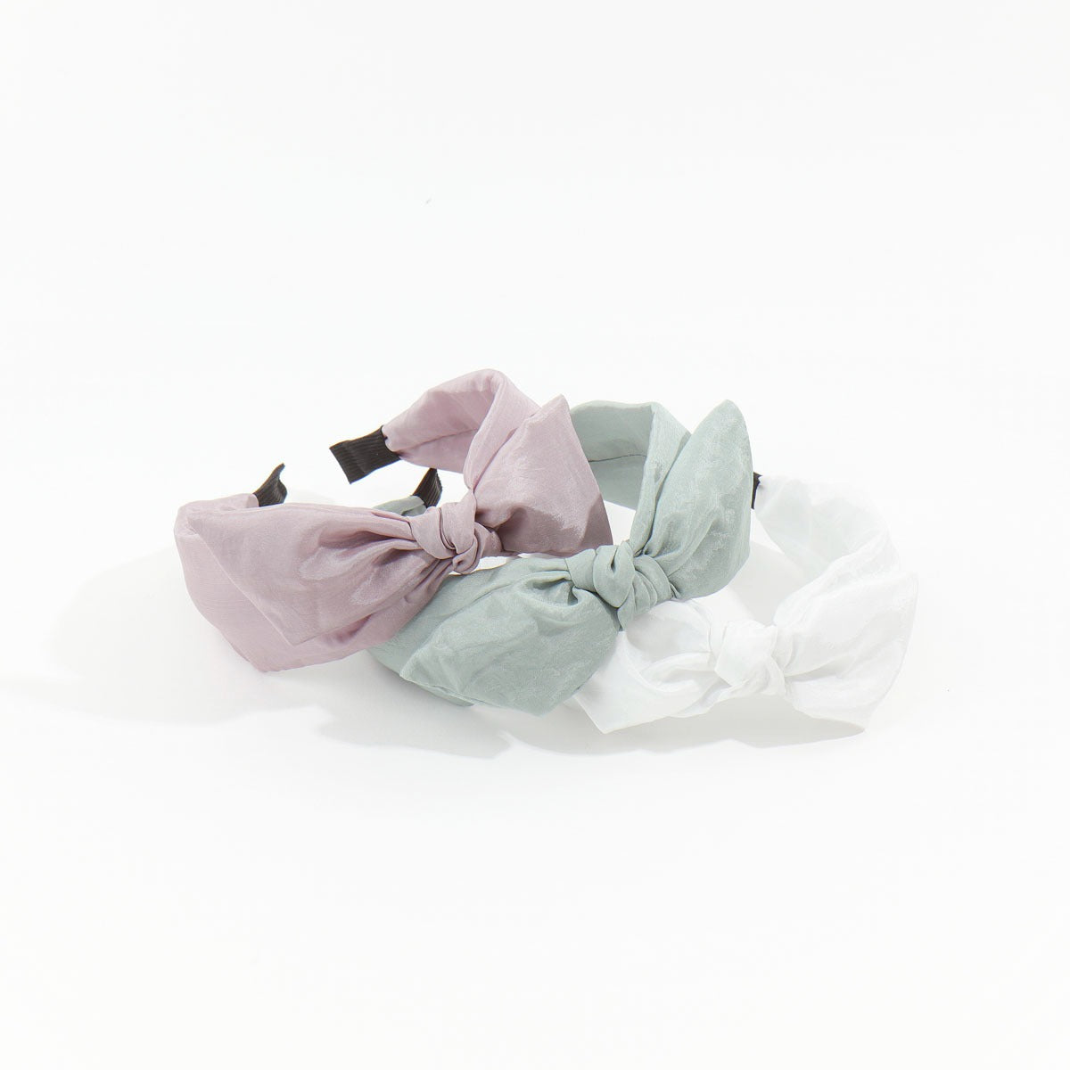 Three trendy soft satin headbands in dusty mauve, sage green, and white featuring an elegant top knot bow design.