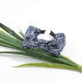 A dark blue bandana print knotted bow headband resting stylishly on top of a long green faux plant stem against a white background.