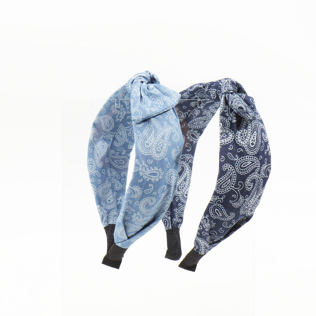 Two paisley bandana headbands, one light blue and one dark navy blue, displayed upright side-by-side on a clear acrylic stand.