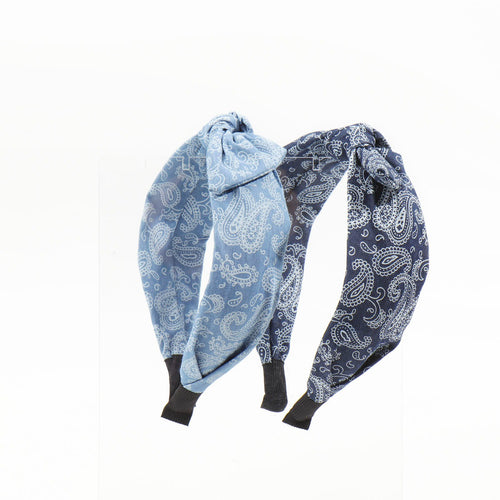 Two paisley bandana headbands, one light blue and one dark navy blue, displayed upright side-by-side on a clear acrylic stand.