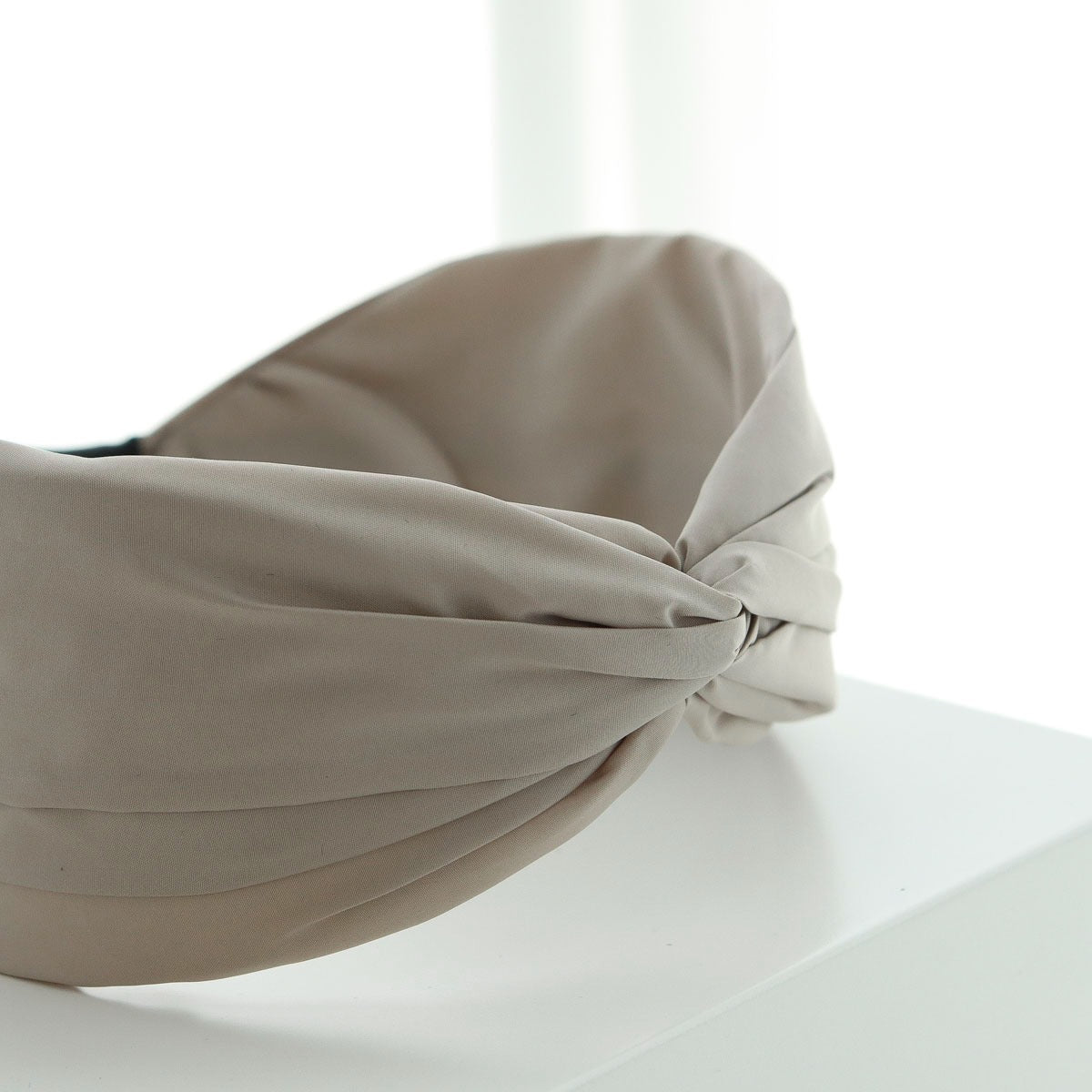 Close-up detail of the elegant front twist knot on a soft beige fabric headband displayed on a white surface.