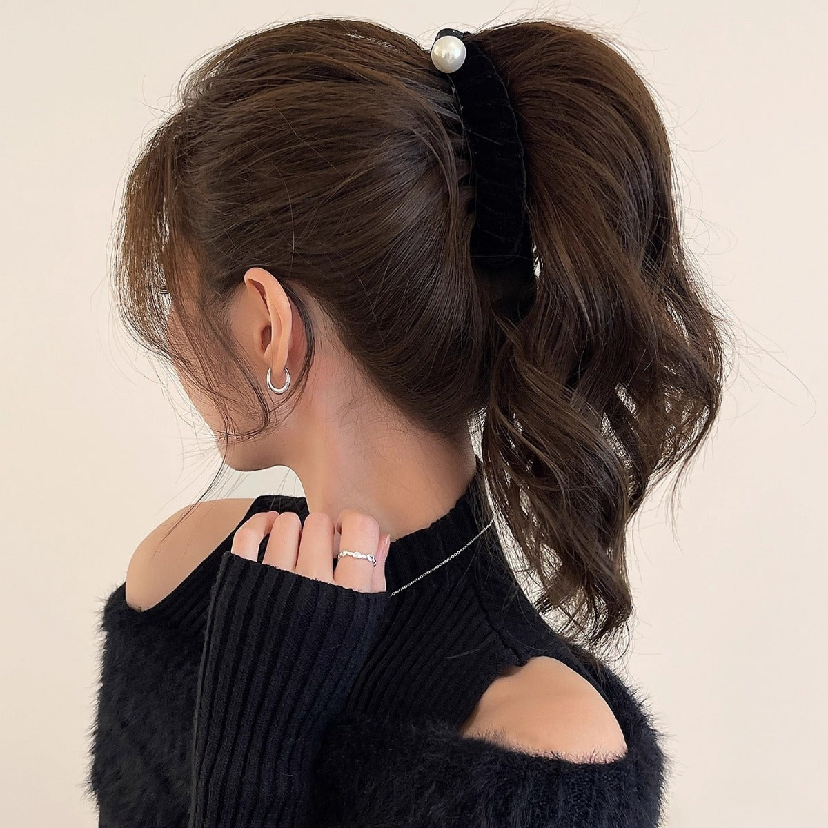 Back profile of a woman with thick, wavy brown hair styled in a high ponytail using a vertical black velvet and pearl banana hair clip.
