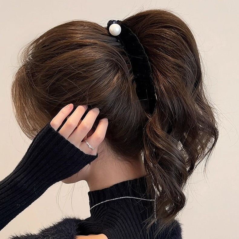 Close-up side view of a woman wearing a black fuzzy cutout sweater, elegantly holding her neck with her hair styled in a ponytail using a black velvet pearl banana clip.