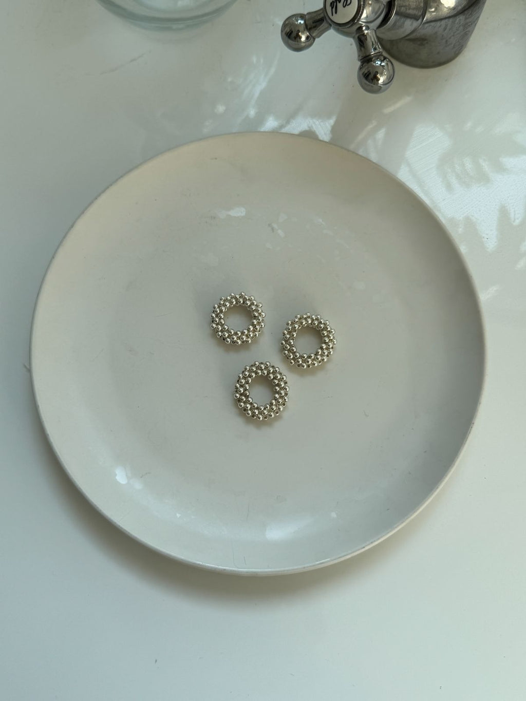 Top-down view of three shiny silver elastic bubble rings displayed on a simple, off-white ceramic plate.