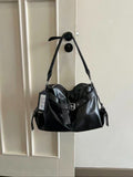 A black soft leather slouchy hobo bag with a front belt buckle strap and graphic tag hanging from a black door handle on a white door.