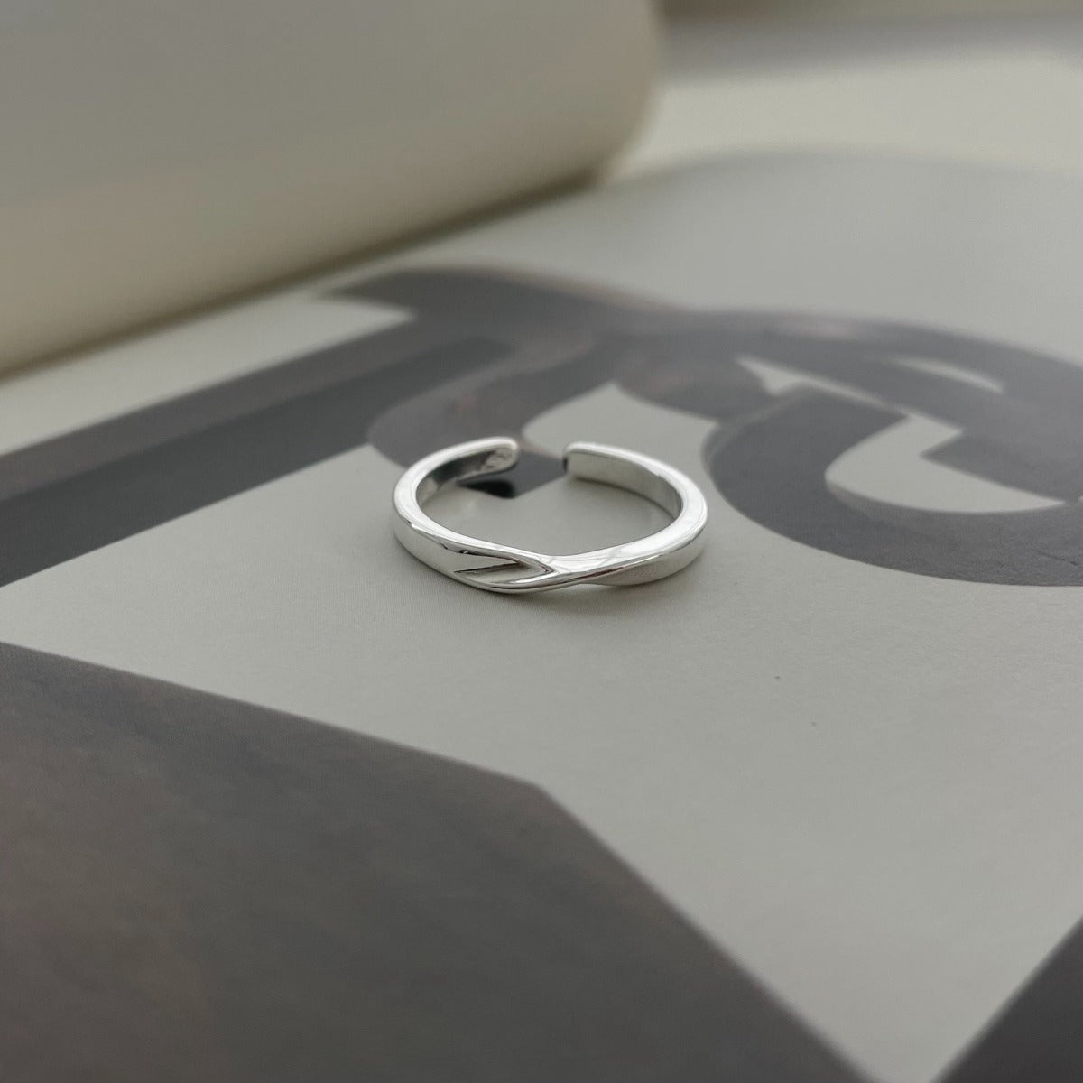A minimalist silver twisted open band ring resting elegantly on an open magazine featuring bold, abstract typography.