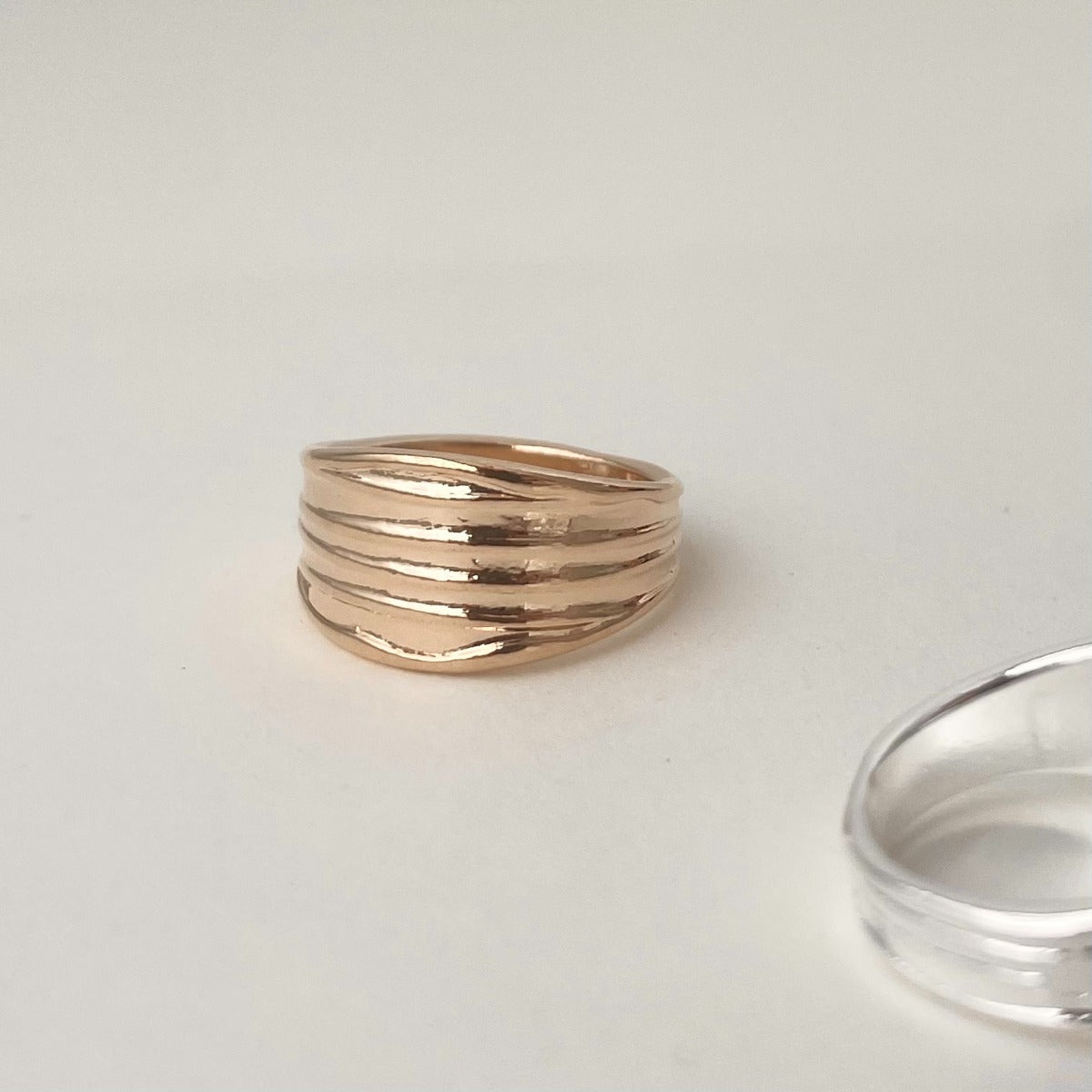 Top-down view of a chunky gold pleated dome ring pinched elegantly inside the folds of crisp white fabric.