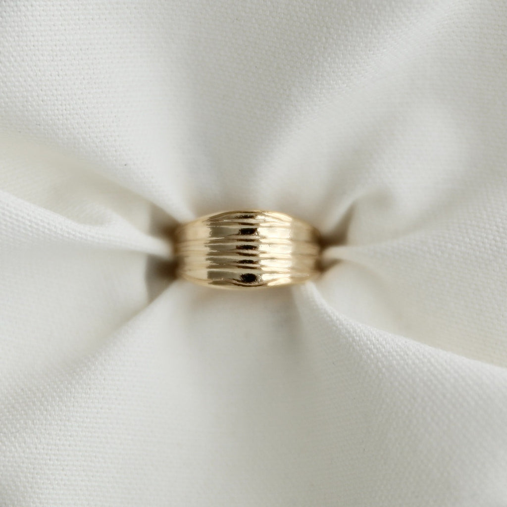 Top-down view of a chunky gold pleated dome ring pinched elegantly inside the folds of crisp white fabric.