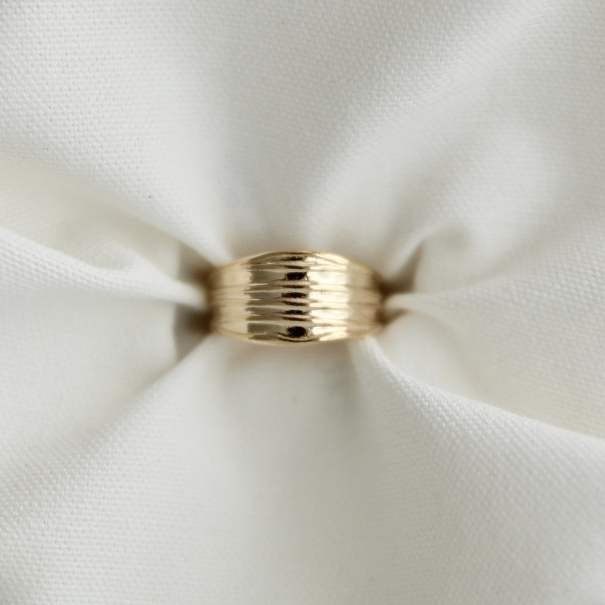 Top-down view of a chunky gold pleated dome ring pinched elegantly inside the folds of crisp white fabric.