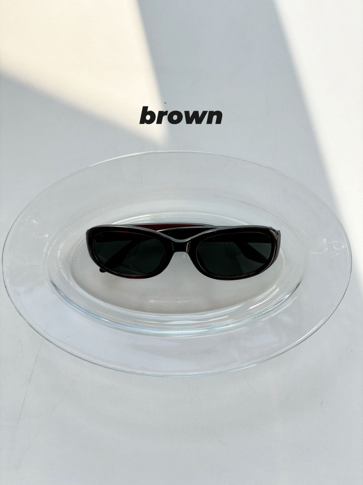 Black sunglasses on a white surface with 'brown' text above.