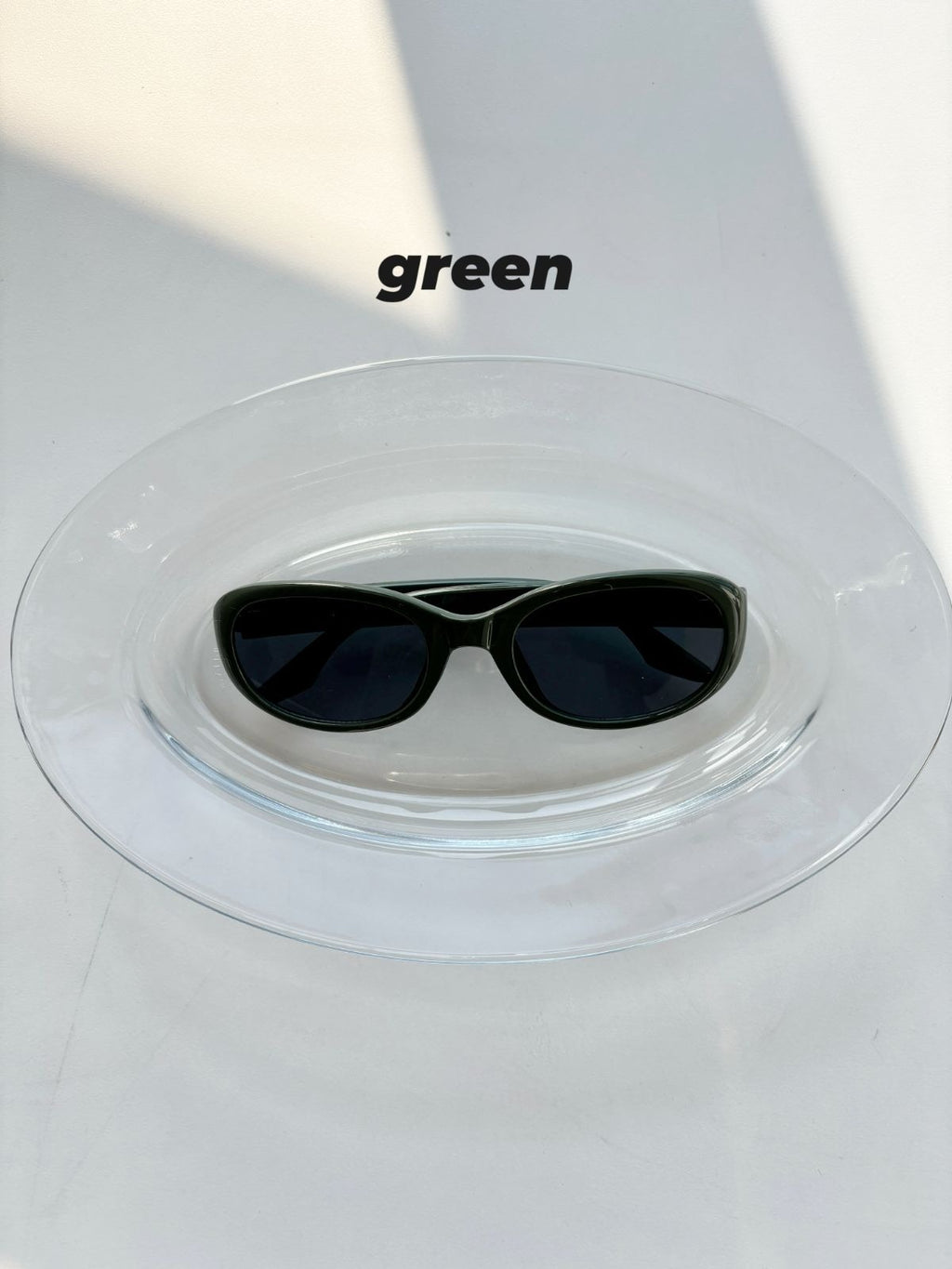 Green sunglasses on a clear stand with 'green' text above.