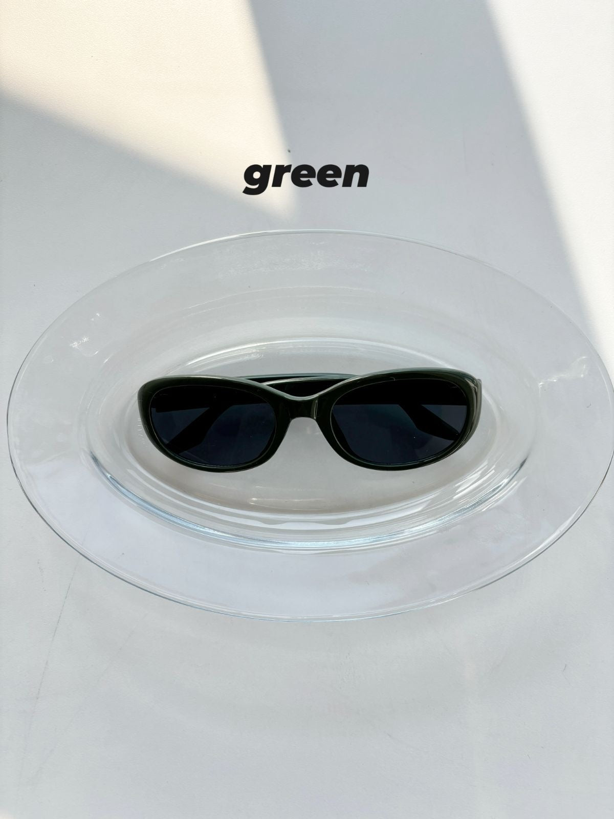 Green sunglasses on a clear stand with 'green' text above.