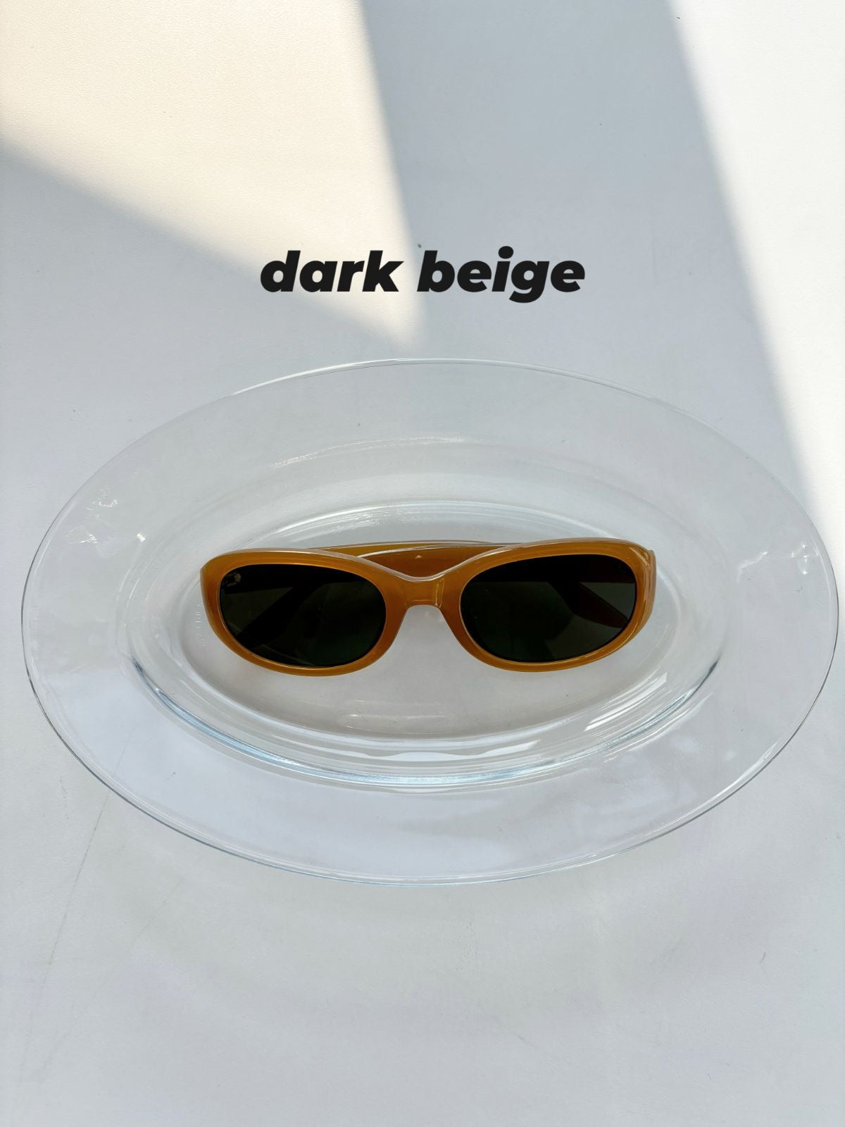 Dark beige sunglasses on a clear dish with a white background